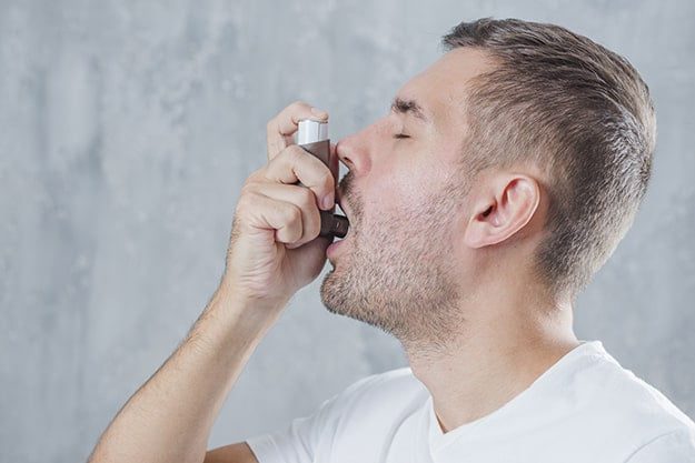 portrait young man using asthma inhaler against grey background